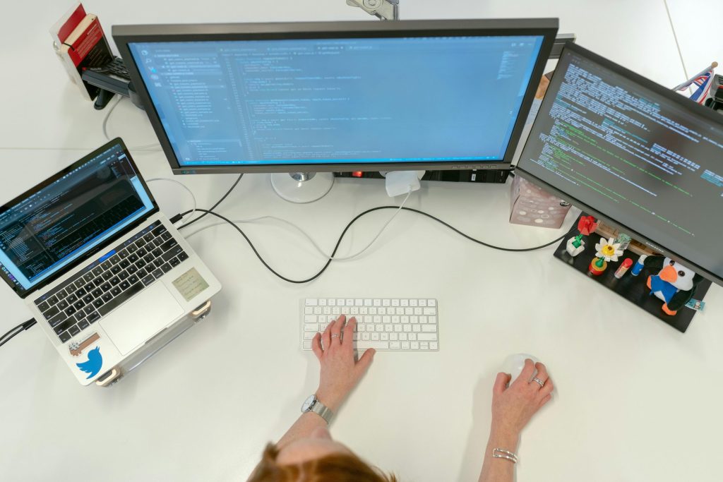 Person working on a computer setup with three screens displaying code and system logs